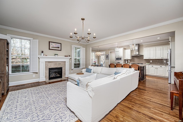 living area with a chandelier, a tiled fireplace, wood finished floors, and crown molding