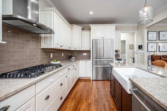 kitchen with stainless steel appliances, ornamental molding, a sink, wood finished floors, and wall chimney exhaust hood