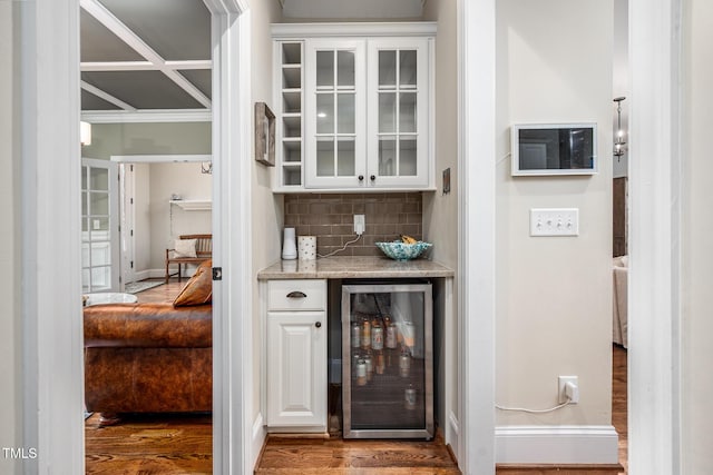 bar with beverage cooler, backsplash, baseboards, and wood finished floors