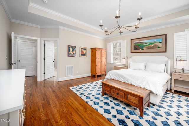 bedroom with a tray ceiling, crown molding, visible vents, wood finished floors, and baseboards