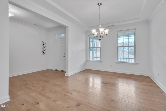 spare room featuring an inviting chandelier, crown molding, light wood-type flooring, and a raised ceiling