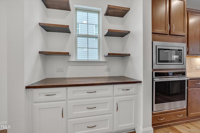 kitchen with open shelves, stainless steel appliances, dark countertops, and light wood finished floors