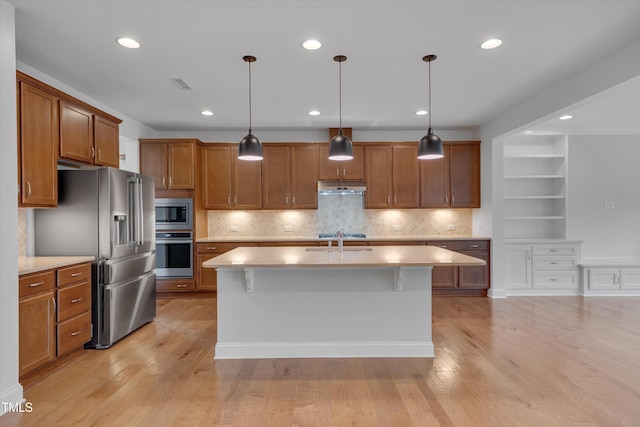 kitchen featuring brown cabinetry, visible vents, a sink, under cabinet range hood, and appliances with stainless steel finishes