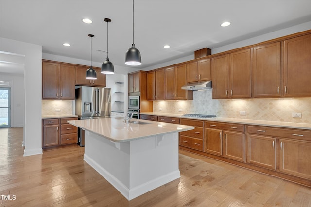 kitchen featuring light wood finished floors, a sink, stainless steel appliances, under cabinet range hood, and brown cabinets