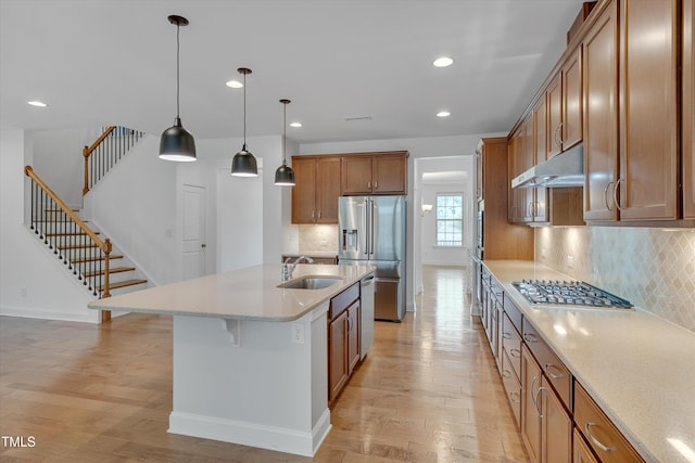 kitchen with brown cabinetry, a sink, under cabinet range hood, appliances with stainless steel finishes, and light wood-type flooring