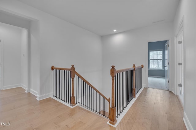 corridor with light wood-type flooring, an upstairs landing, and baseboards