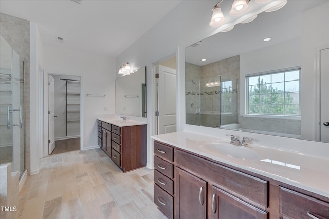 full bathroom with a walk in closet, two vanities, a stall shower, and a sink