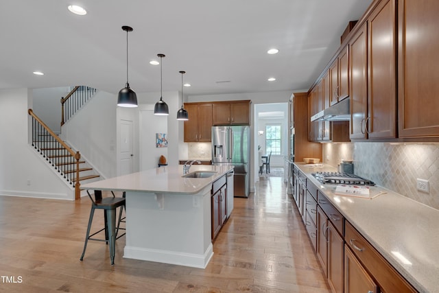 kitchen with under cabinet range hood, light wood finished floors, brown cabinets, and a sink