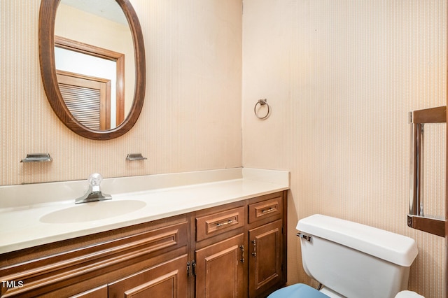 bathroom featuring toilet, wallpapered walls, and vanity