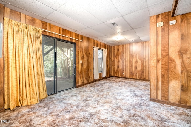 empty room with carpet, wooden walls, visible vents, and a drop ceiling