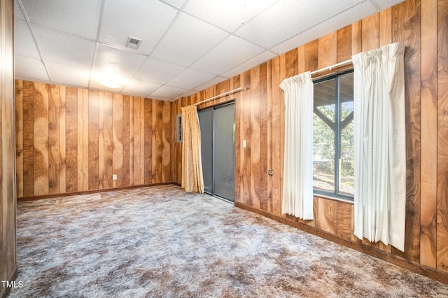 carpeted spare room with wood walls, a drop ceiling, and visible vents