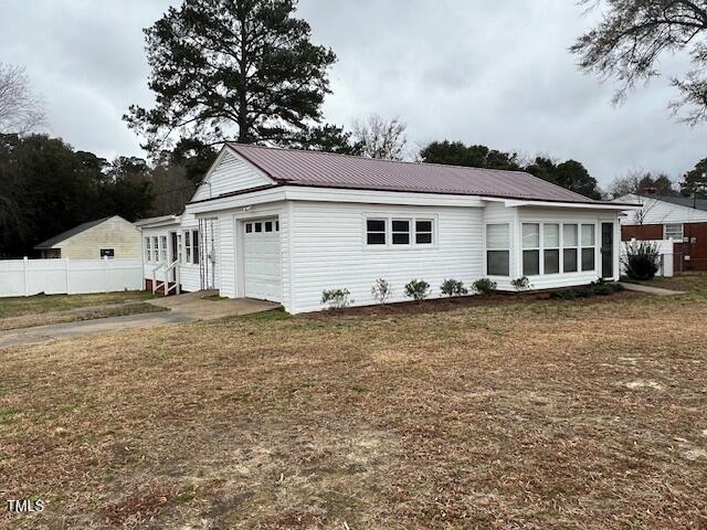 exterior space with an attached garage, a front yard, entry steps, metal roof, and fence