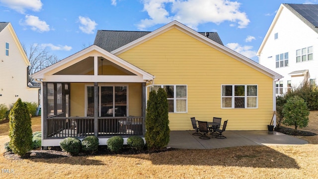 rear view of property with a sunroom, roof with shingles, and a patio