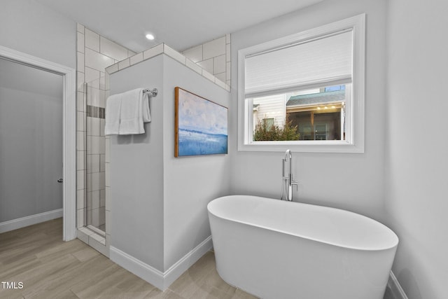 bathroom featuring recessed lighting, wood finished floors, a freestanding tub, tiled shower, and baseboards