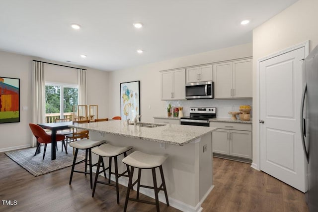 kitchen featuring a center island with sink, dark wood finished floors, a kitchen breakfast bar, stainless steel appliances, and a sink