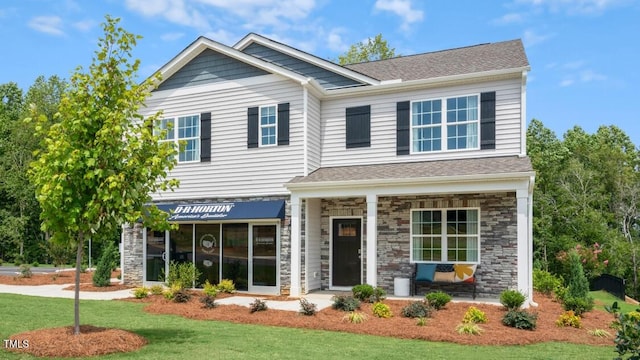 craftsman-style house featuring stone siding, a front lawn, covered porch, and roof with shingles