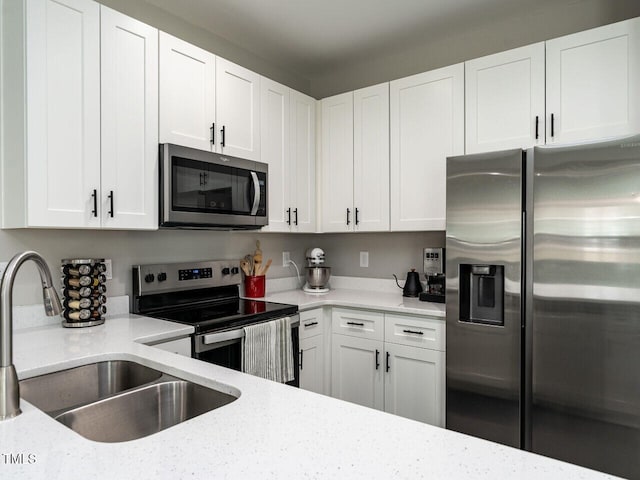 kitchen featuring appliances with stainless steel finishes, white cabinetry, a sink, and light stone countertops