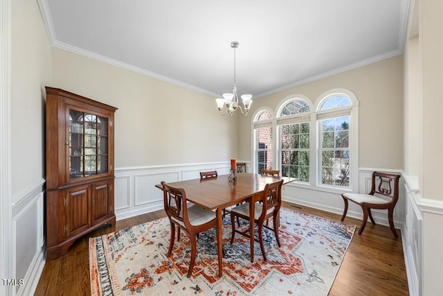 dining space with wood finished floors, wainscoting, crown molding, and an inviting chandelier