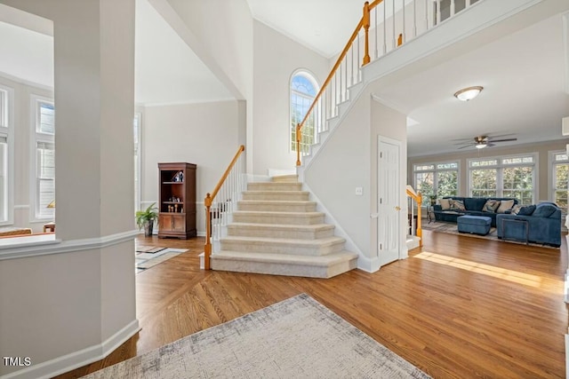 stairway featuring ornamental molding, wood finished floors, a towering ceiling, and baseboards