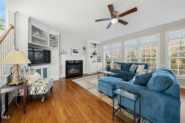 living area featuring a fireplace with flush hearth, wood finished floors, and crown molding