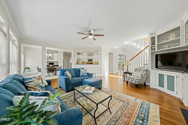 living room with built in features, a ceiling fan, ornamental molding, wood finished floors, and stairs