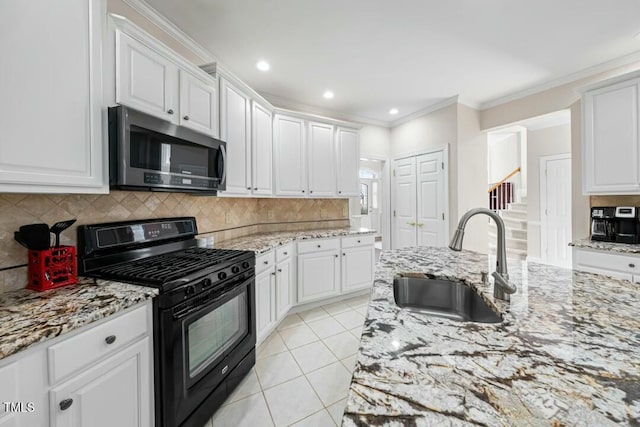 kitchen with black range with gas cooktop, a sink, white cabinets, backsplash, and stainless steel microwave