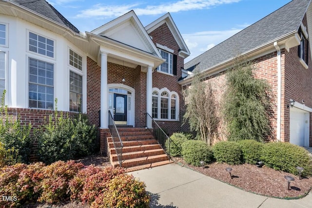 entrance to property with brick siding, roof with shingles, and an attached garage