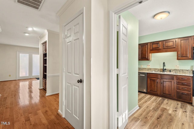 corridor featuring visible vents, a sink, light wood-style flooring, and baseboards