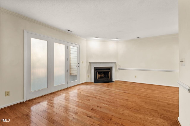 unfurnished living room with visible vents, a fireplace with flush hearth, ornamental molding, wood finished floors, and baseboards