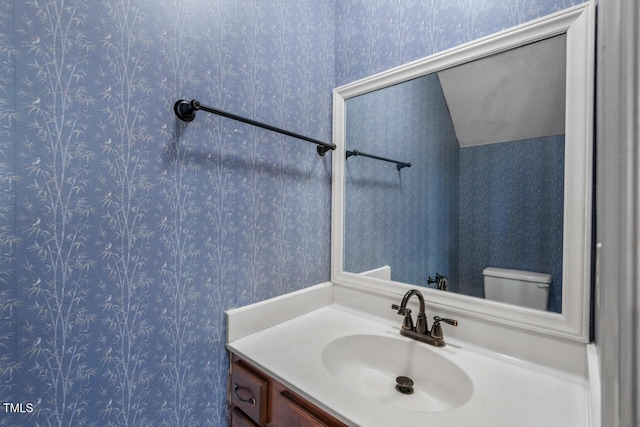 bathroom featuring toilet, wallpapered walls, and vanity