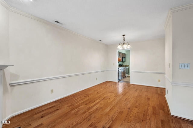 unfurnished room featuring ornamental molding, visible vents, an inviting chandelier, and wood finished floors