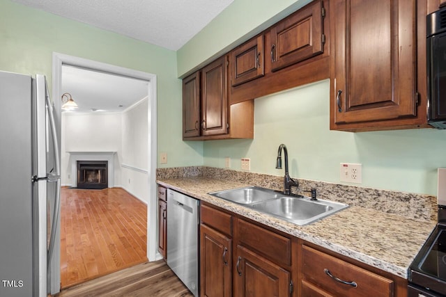 kitchen with a textured ceiling, stainless steel appliances, a fireplace with flush hearth, a sink, and light wood finished floors