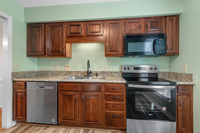 kitchen featuring stainless steel appliances, a sink, light wood-style flooring, and light stone counters