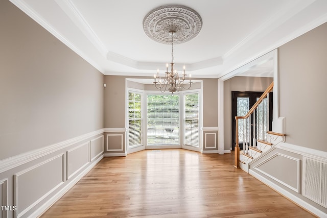 unfurnished dining area with a tray ceiling, a decorative wall, stairway, an inviting chandelier, and light wood-style floors