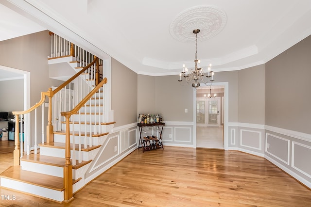 interior space with a chandelier, a decorative wall, wood finished floors, ornamental molding, and a tray ceiling