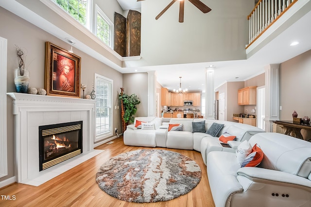 living area with a towering ceiling, ornamental molding, light wood-type flooring, a fireplace, and ceiling fan with notable chandelier