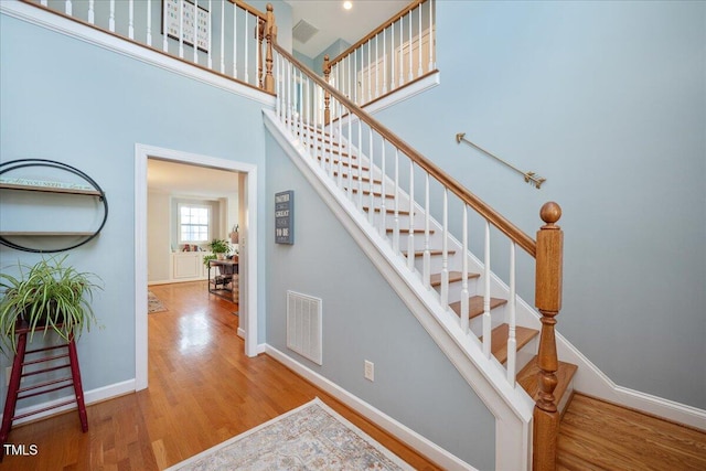 stairs with visible vents, baseboards, wood finished floors, and a towering ceiling