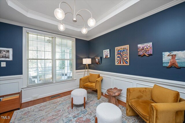 living area with a tray ceiling, wood finished floors, visible vents, and wainscoting