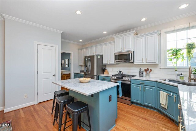 kitchen featuring blue cabinetry, a kitchen island, light wood-style flooring, appliances with stainless steel finishes, and a sink