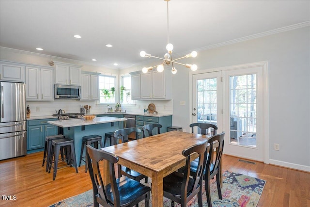 dining room featuring visible vents, baseboards, light wood-type flooring, ornamental molding, and a notable chandelier