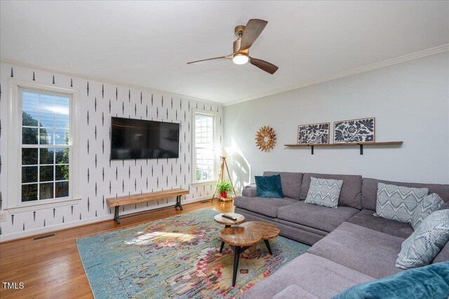 living area featuring visible vents, wallpapered walls, crown molding, baseboards, and wood finished floors