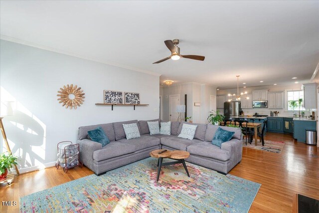 living area featuring visible vents, light wood-style flooring, ceiling fan with notable chandelier, crown molding, and baseboards