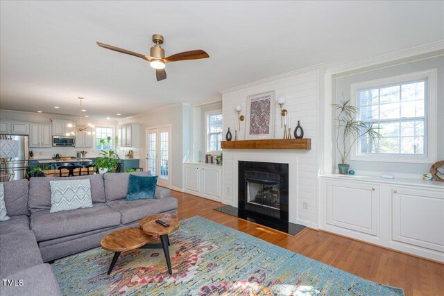 living area featuring ceiling fan with notable chandelier, a fireplace, wood finished floors, and ornamental molding