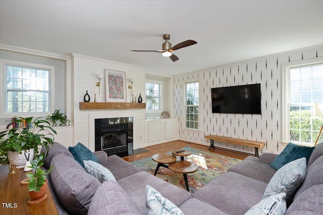 living area featuring a ceiling fan, wood finished floors, wallpapered walls, a fireplace, and crown molding