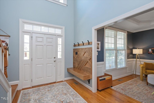 entrance foyer with a wainscoted wall, ornamental molding, visible vents, and wood finished floors