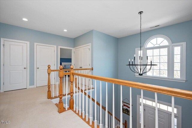 hall featuring visible vents, carpet floors, an upstairs landing, recessed lighting, and an inviting chandelier