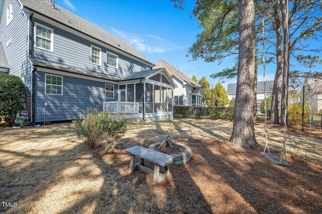 rear view of property featuring a fire pit and a sunroom