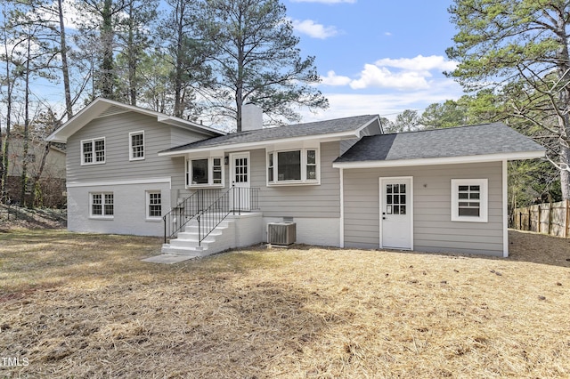 rear view of house featuring central AC unit, fence, a yard, a shingled roof, and a chimney