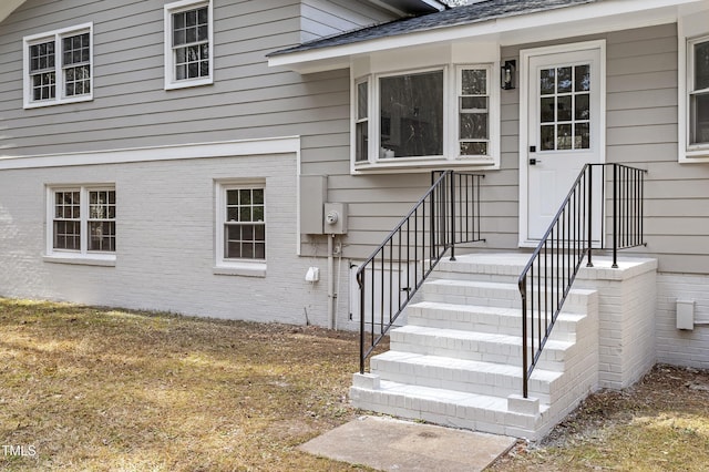 view of exterior entry featuring brick siding and a shingled roof