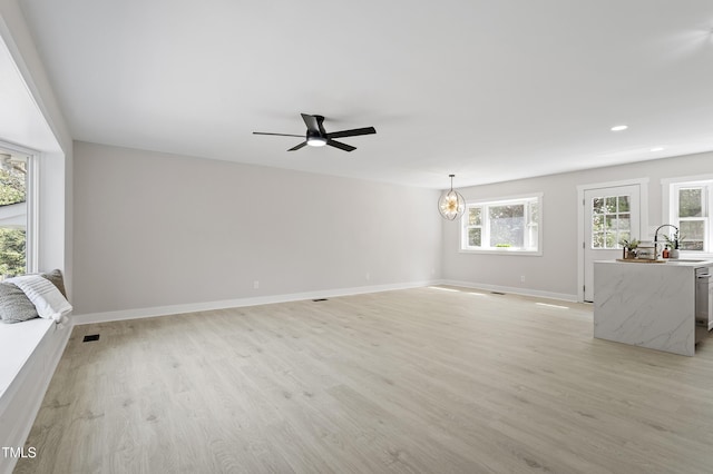 unfurnished living room with light wood-style flooring, recessed lighting, ceiling fan with notable chandelier, and baseboards